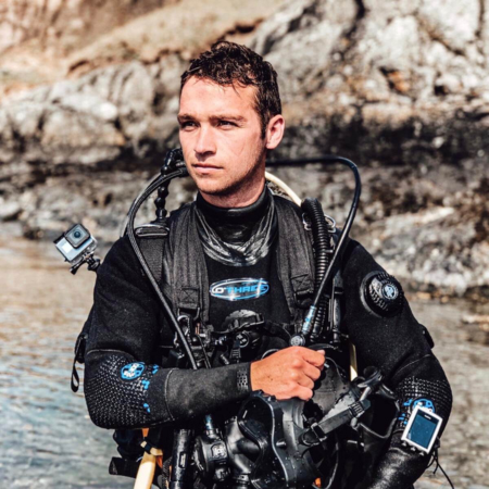 Jake is standing by the edge of the sea. He is wearing diving gear.